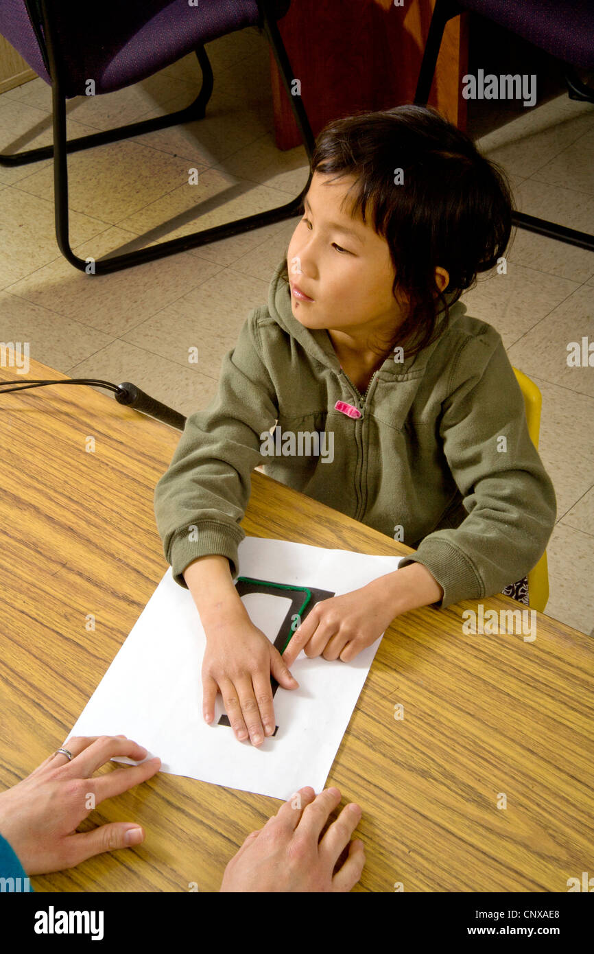 Ein blindes Mädchen asiatische amerikanische berührt einen Buchstaben "L" in erhöhten Typ in einem speziellen braucht schreiben Klasse für Blinde. Stockfoto