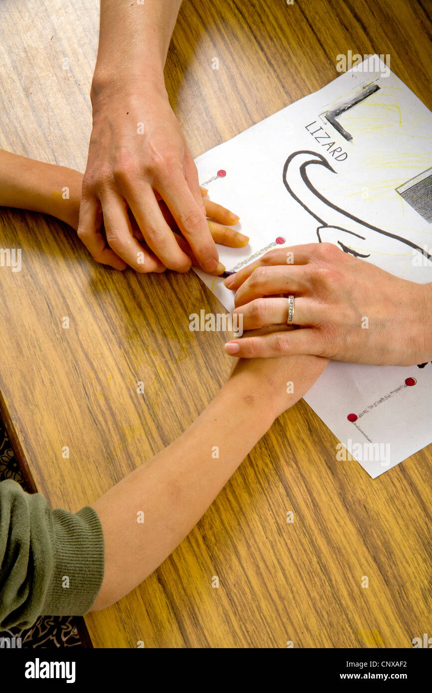 Ein Lehrer führt ein blindes Kind Hände über den Umriss einer Eidechse in erhöhten Art in einem besonderen Bedürfnissen, die Klasse zu schreiben. Stockfoto