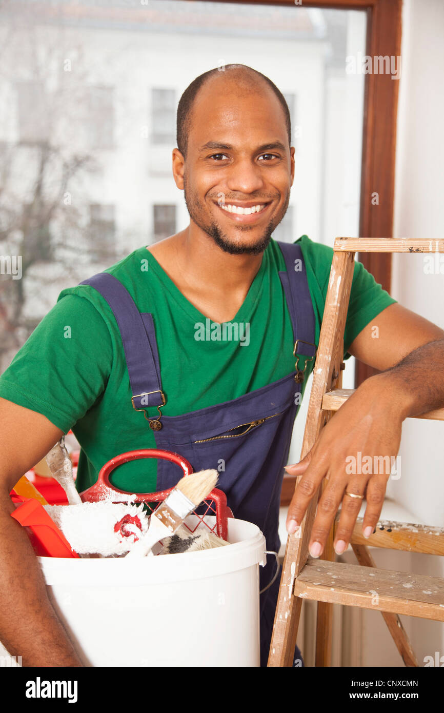 Ein Mann hält einen Eimer mit Farbe versorgt stützte sich auf eine Leiter Stockfoto