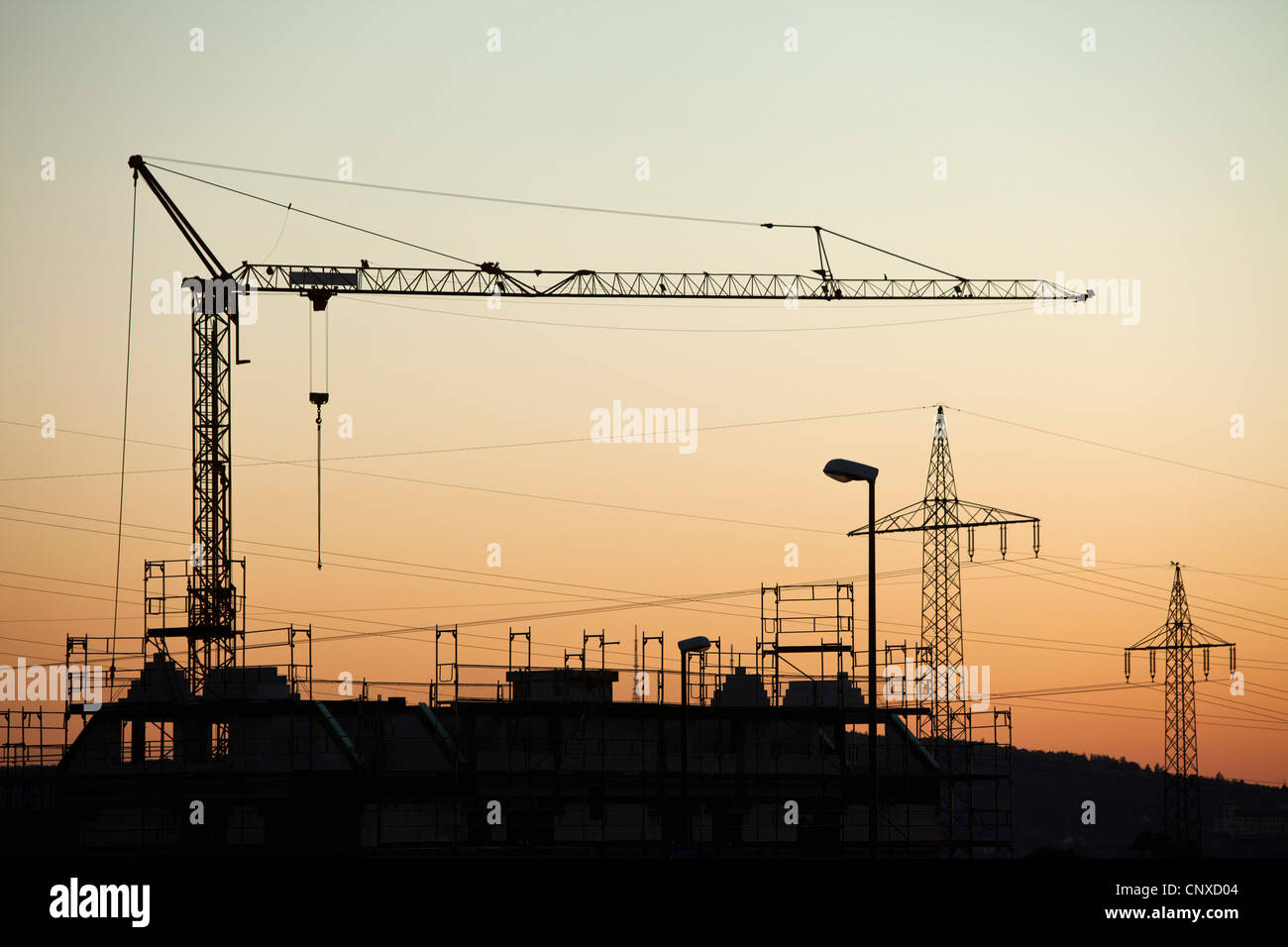 Ein Bau Kran und Elektrizität Masten Silhouette gegen Sonnenuntergang Himmel Stockfoto