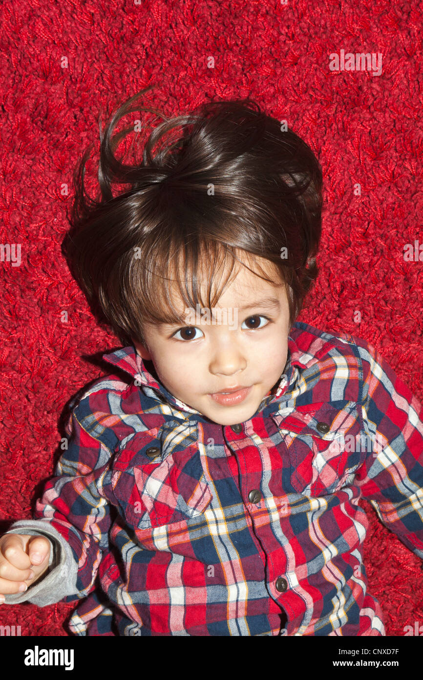 Ein kleiner Junge auf einem roten Teppich liegend Stockfoto
