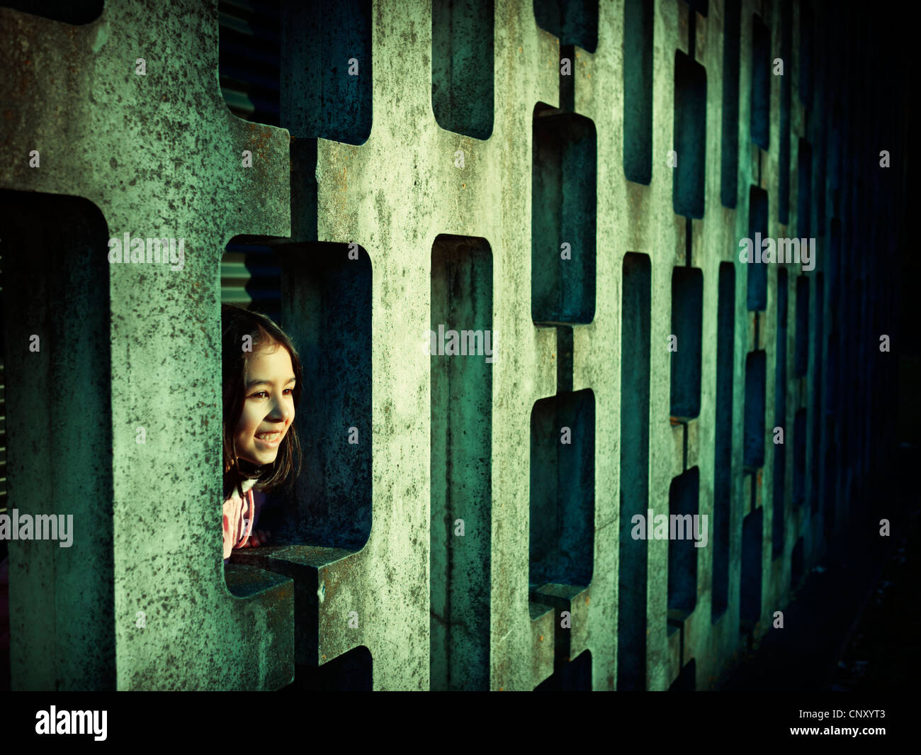 Mädchen sieht durch gemusterte Betonblock Wand Stockfoto