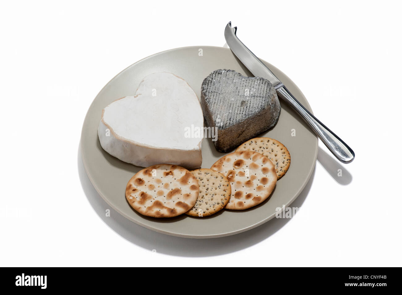 Zwei Käsesorten mit Crackern und Käsemesser auf einem Teller in Herzform Stockfoto