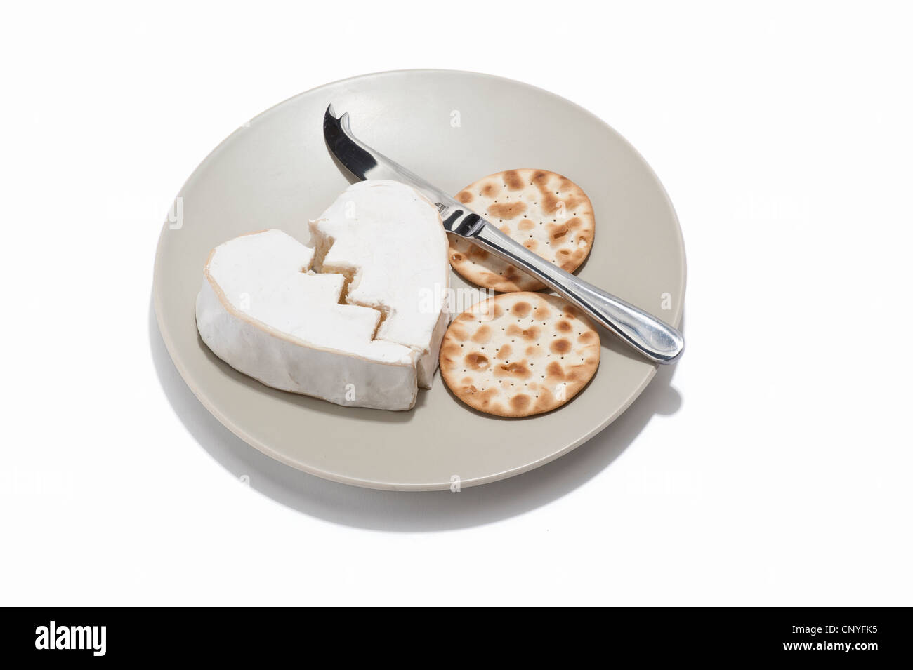 Ein gebrochenes Herz geformten Käse mit Crackern und Käsemesser auf einem Teller Stockfoto