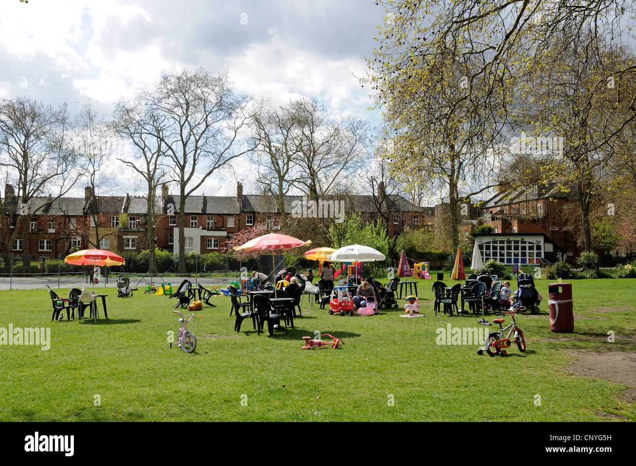 Eltern mit Kindern rund um s Cafe geben Sonnenschirm Stühle Highbury Fields mit 02:00 Club im Hintergrund Stockfoto