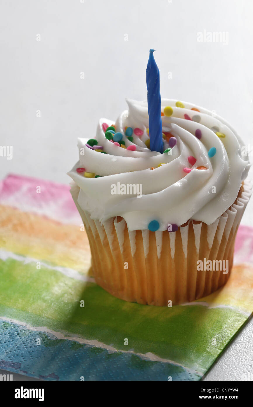 Ein Vanille Cupcake, gefrostet und verziert mit einem blauen Geburtstag Kerze und platziert auf einer bunten Serviette mit einem weißen backgrnd Stockfoto