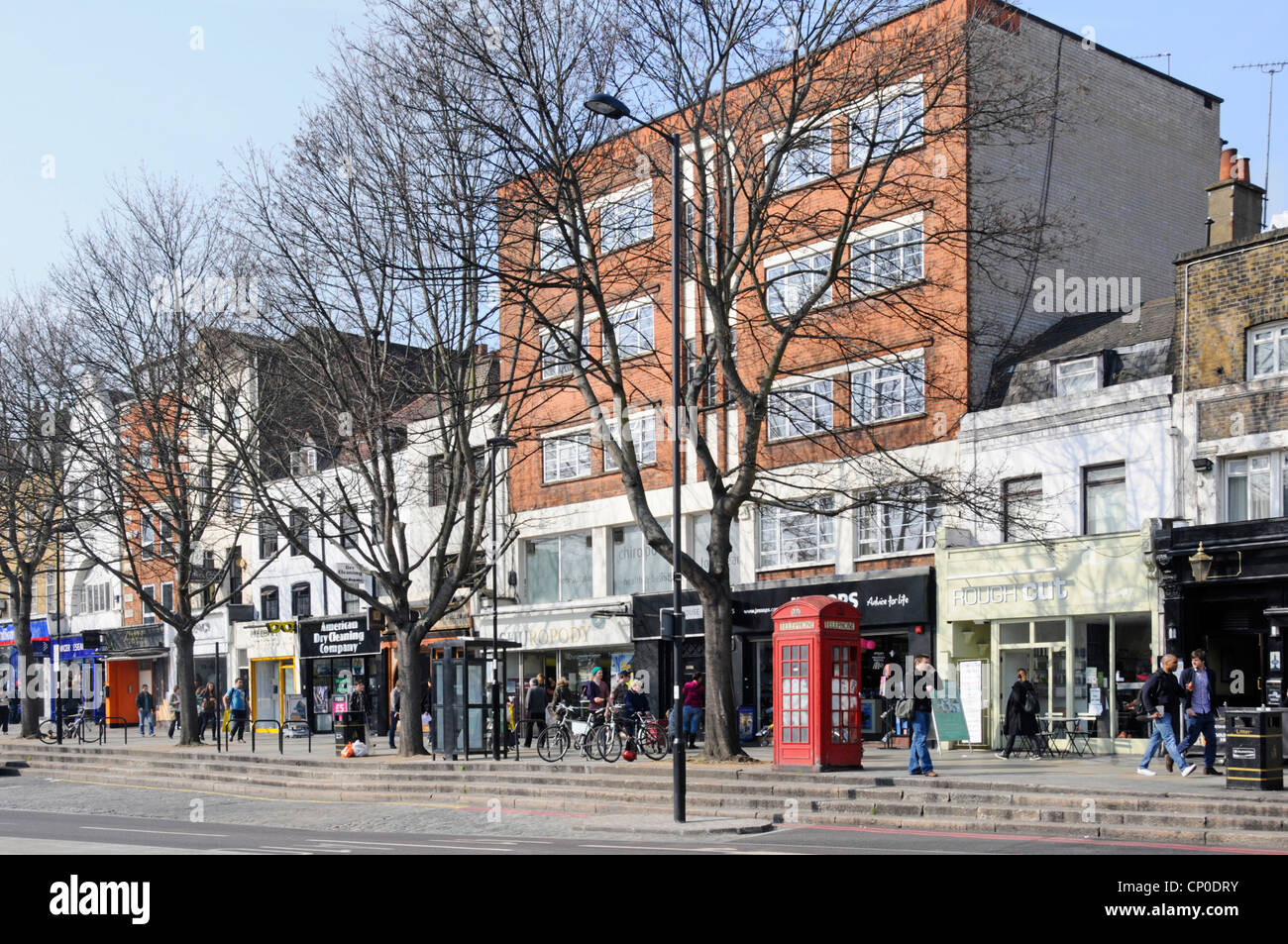 Winter Bäume & Menschen in der Upper Street sonnige Szene einschließlich Einzelhandelsgeschäfte und Geschäftsräume Islington London England Großbritannien Stockfoto