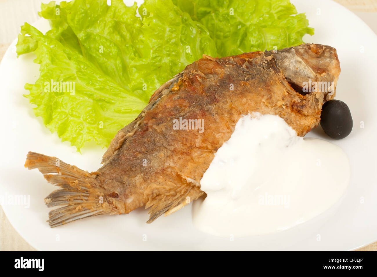 Fisch gebraten Karpfen mit saurer Sahne auf einem Teller mit Salatblättern Stockfoto