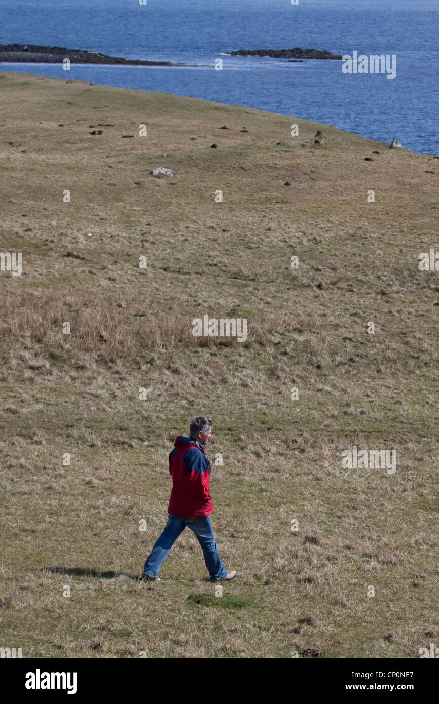 Ein Mann zu Fuß entlang einer Moorlandschaft über dem Meer Stockfoto