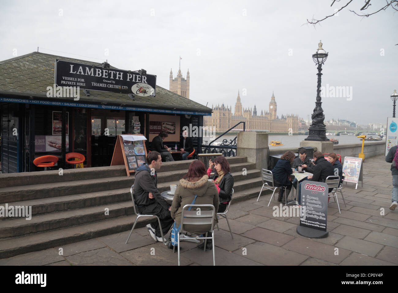 Kleines Café neben Lambeth Pier mit den Houses of Parliament hinter und der Themse, London, Stockfoto