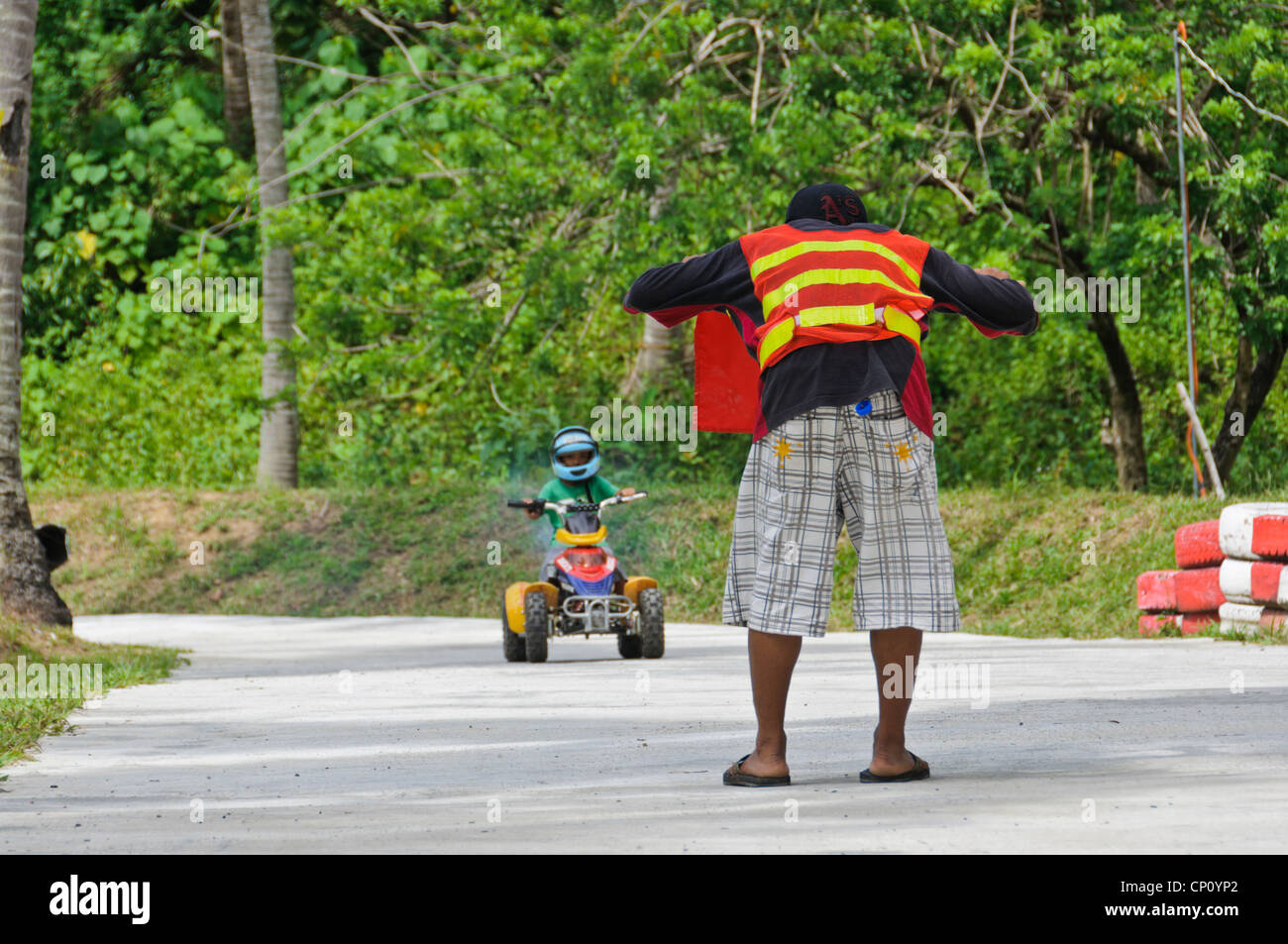 Verfolgen Sie Marschall stoppen kleiner Junge Reiten ATV mit roten Fahne - Adventure Park Puerto Galera Oriental Mindoro Philippinen Asien Stockfoto