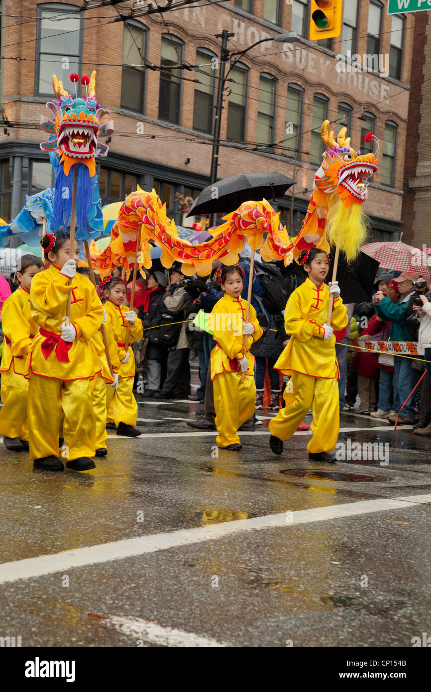 Mädchen und jungen gekleidet in leuchtendem Gelb und rote Trachten tragen lange Drachen, wie sie in die 2012 Vancouver Chines Fuß Stockfoto