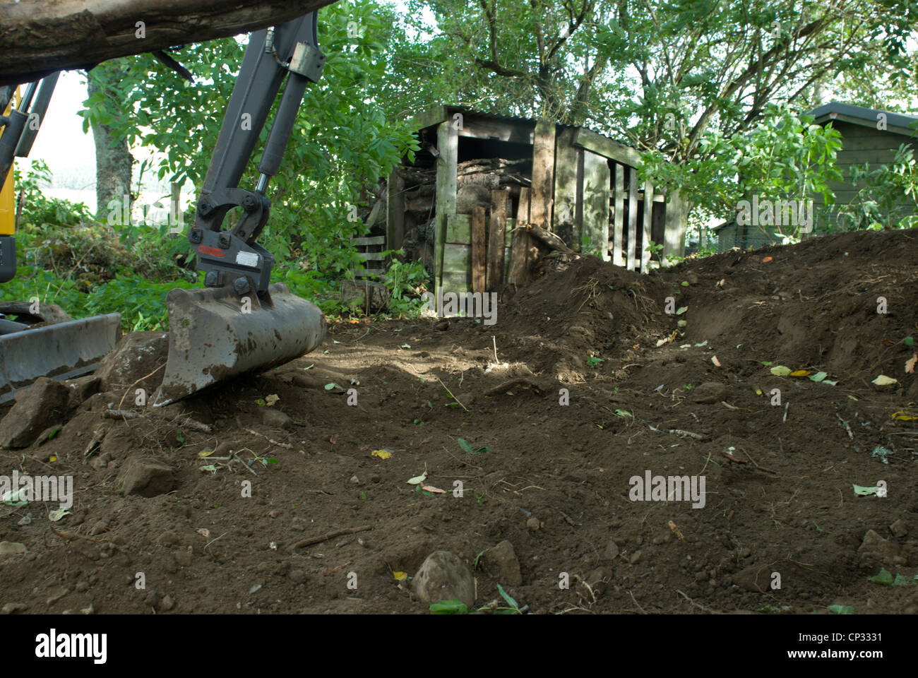 ein Mini-Bagger bei der Arbeit in einem ländlichen Garten den Weg frei für einen Schuppen-Basis Stockfoto