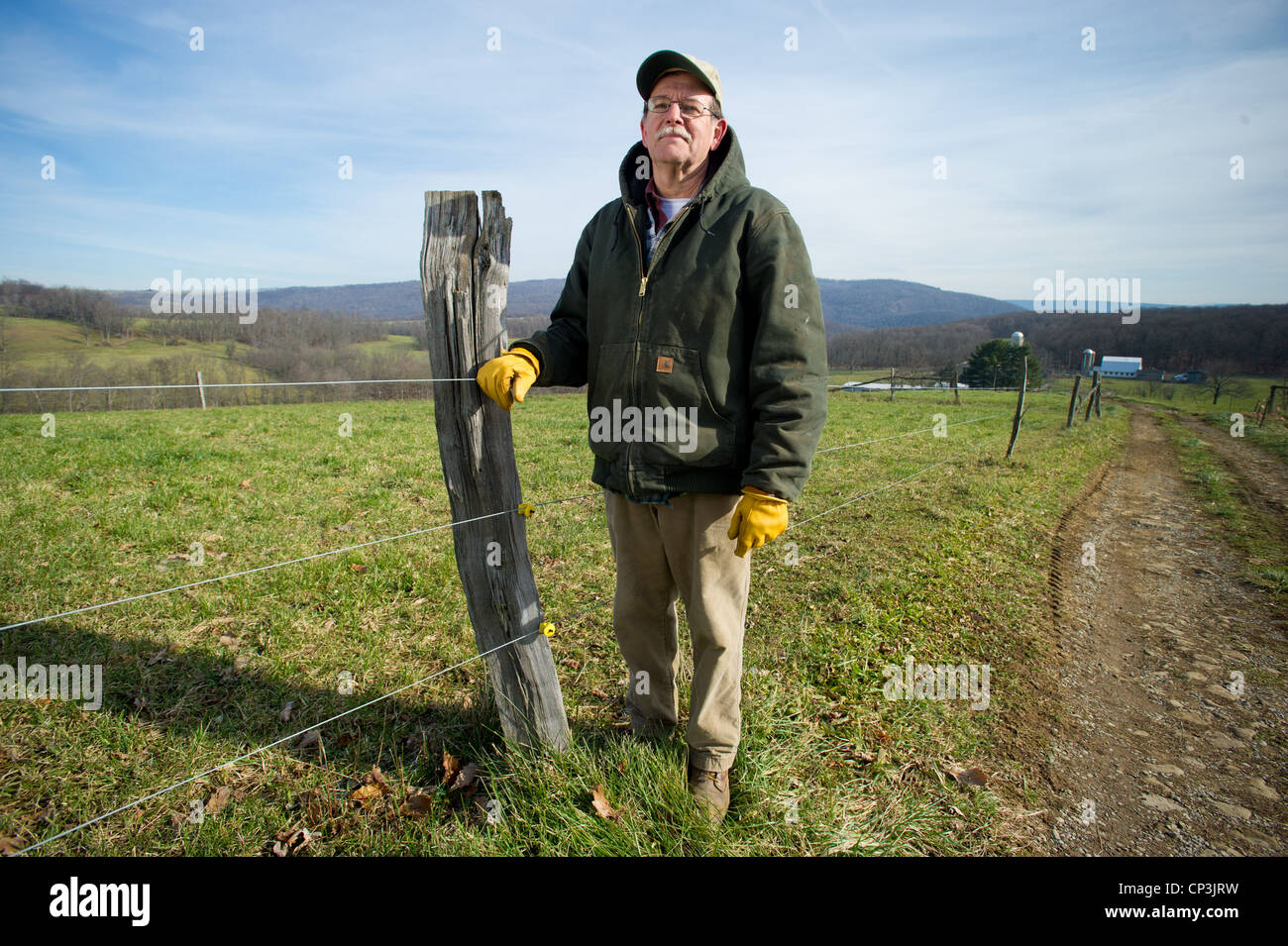 Landwirt steht hoch gegen Holzpfosten mit Blick auf Feld. Stockfoto