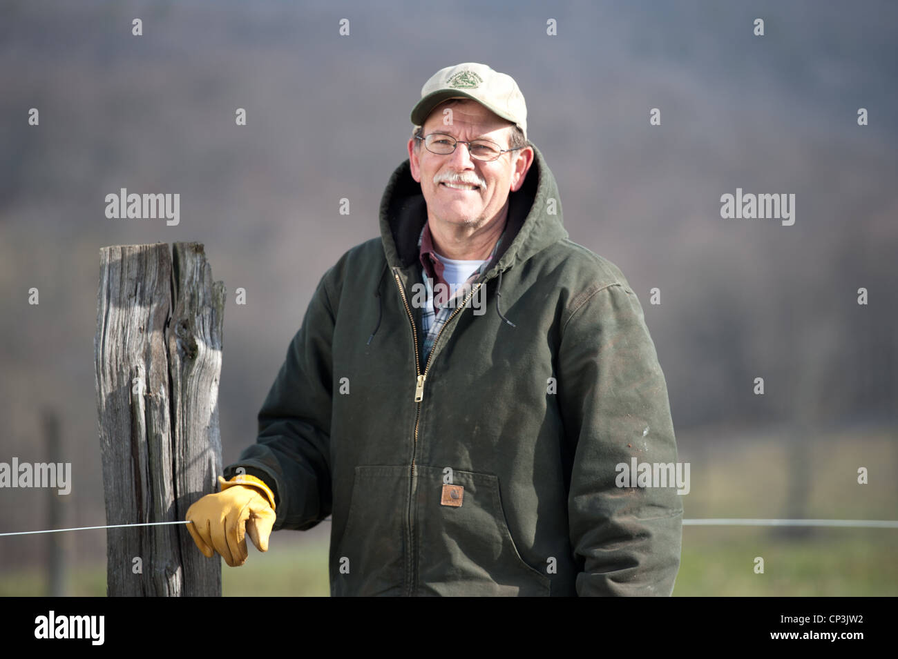 Landwirt steht lächelnd gegen Zaun. Stockfoto