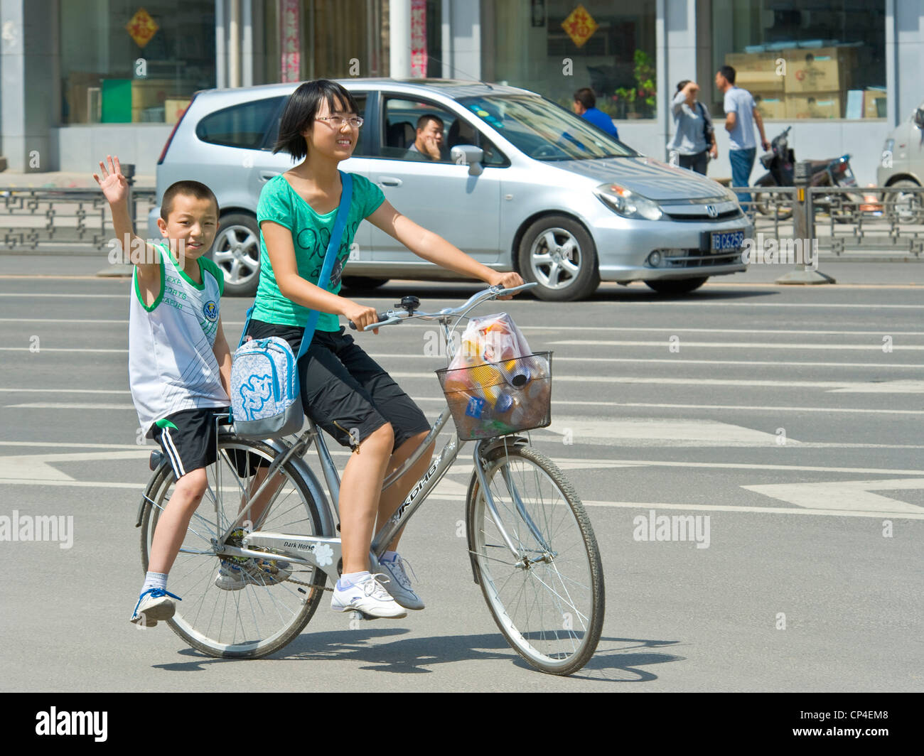 Eine Mutter und ihr Kind Lächeln und winken in die Kamera auf einem Fahrrad fahren entlang einer Hauptstraße in Datong. Stockfoto