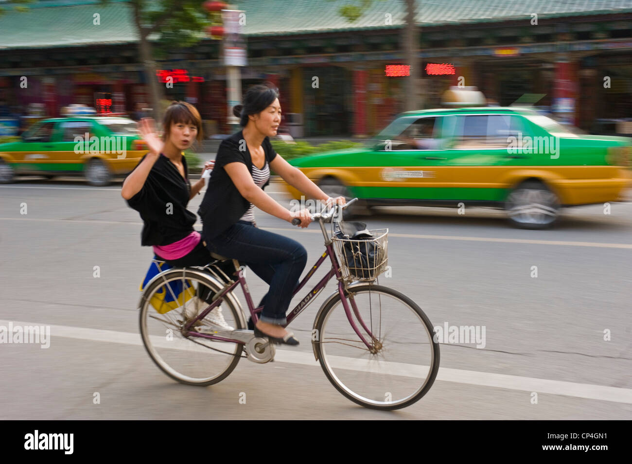2 lokale chinesische Frauen Reiten eines Fahrrades mit einem winken in die Kamera auf den Straßen von Zhongwei. Stockfoto