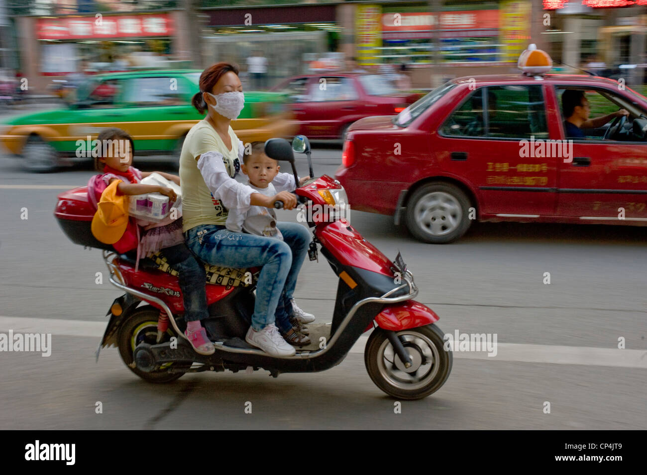 Eine lokale chinesische Dame Reiten ihr Motorroller und 2 Kinder nicht tragen von Sturzhelmen - mit Motion blur. Stockfoto