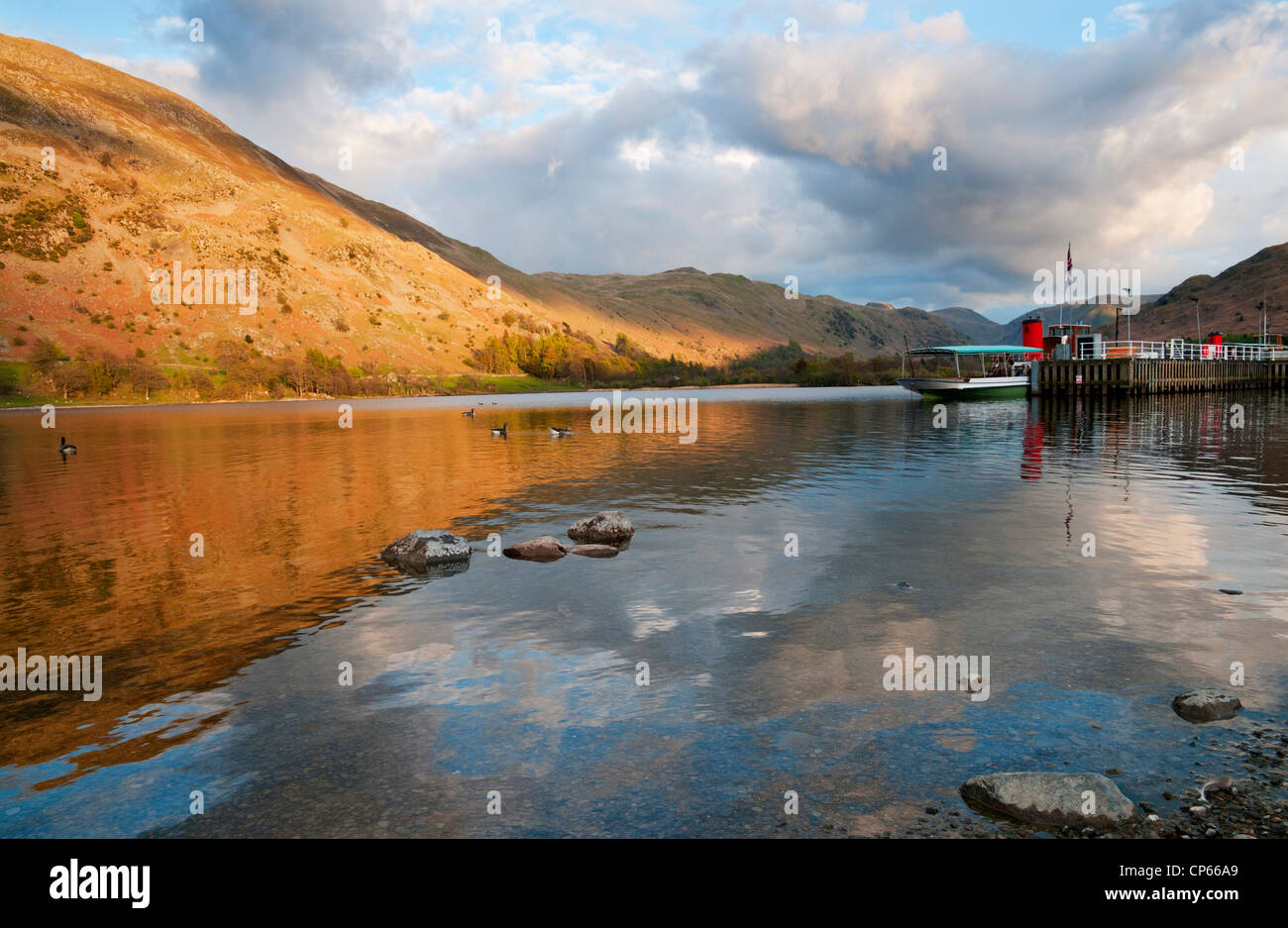 Boote am Glenridding Pier für den Abend, sonnenbeschienenen Fells spiegelt sich im Wasser, Ullswater, Lake District, Cumbria, UK Stockfoto