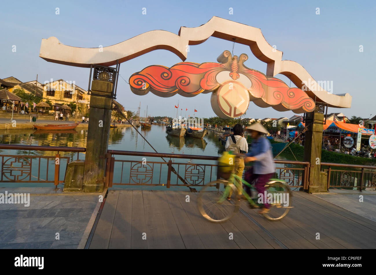 Horizontale Ansicht einer traditionell gekleidete alte Dame Radfahren auf dem Thu Bồn Fluss Klappbrücke Kreuzung im Zentrum von Hoi An, Vietnam. Stockfoto