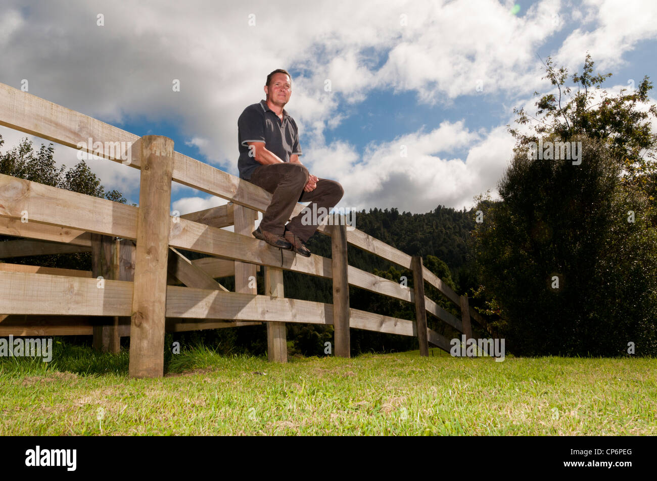 Mann sitzt auf Holzzaun auf seinen Lebensstil Block, Neuseeland Stockfoto