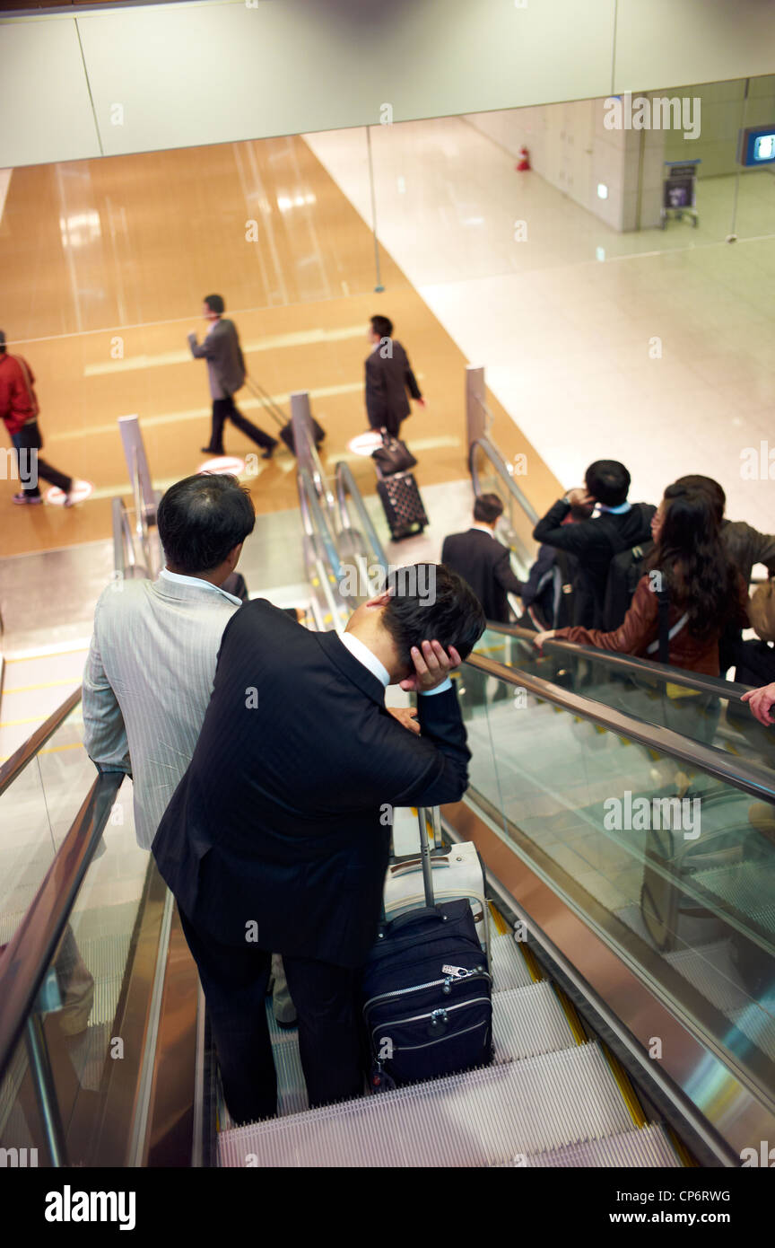 Eine müde koreanische Geschäftsleute auf einer Rolltreppe am Incheon International Airport Stockfoto