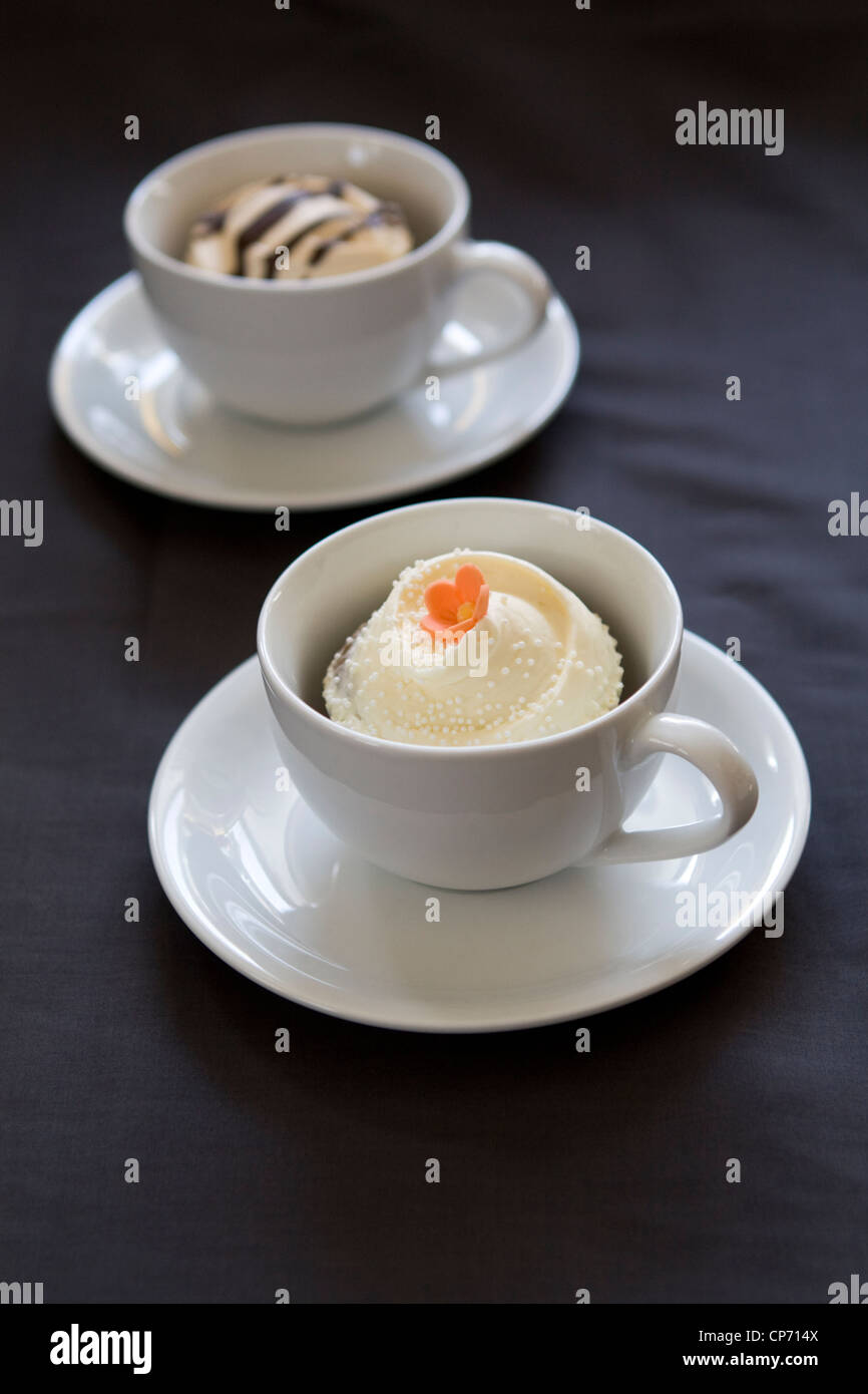 Ein Foto von zwei weißen Tassen mit hausgemachten Muffins auf einem dunklen Hintergrund. Stockfoto