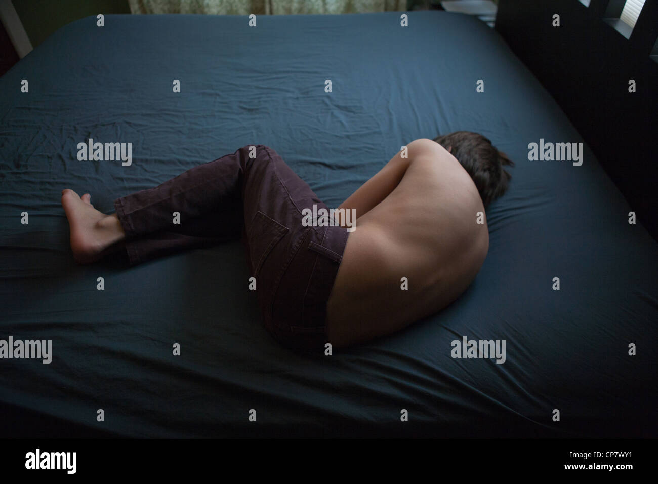 Zwölf Jahre alter Junge auf einem Bett mit Bauchschmerzen. Stockfoto