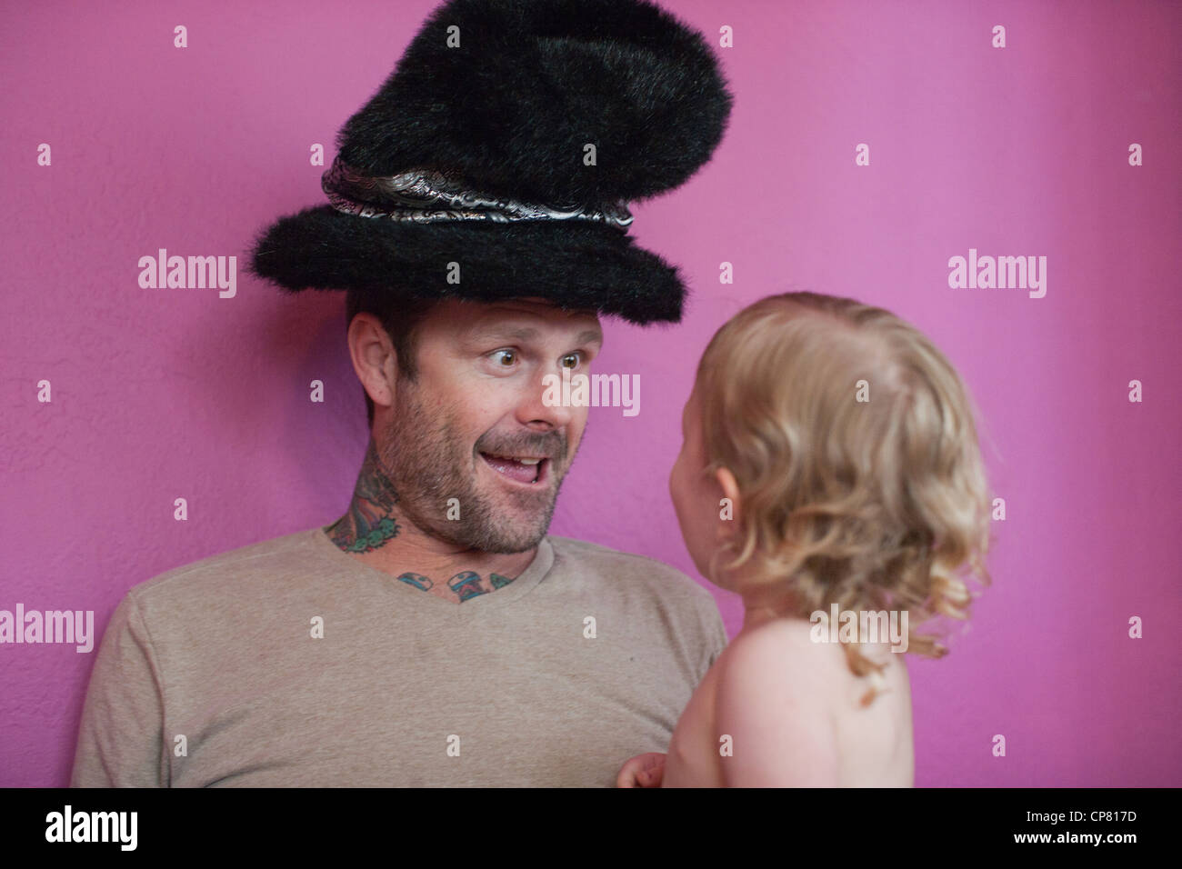 Tätowierte Vater macht ein dummes Gesicht für seine Tochter zu Hause einen lustigen Hut aufsetzen. Stockfoto