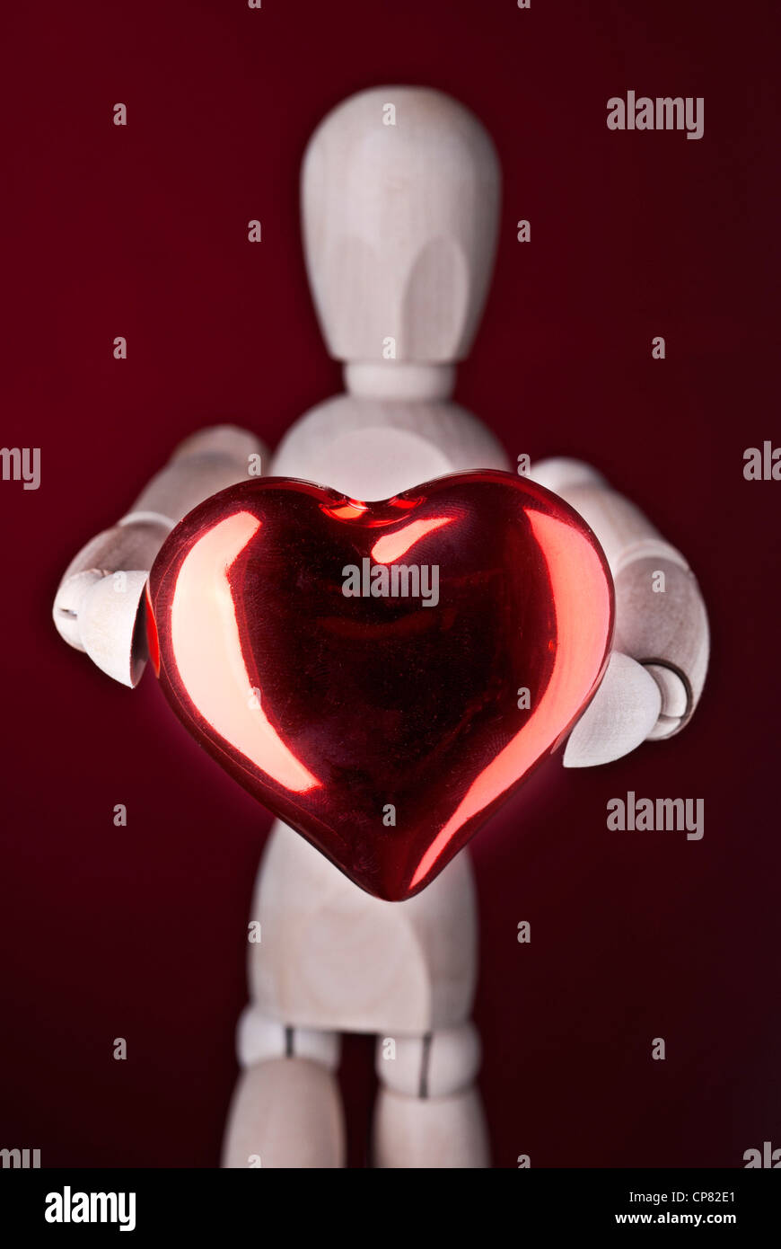 Eine Holzpuppe hält ein rotes Herz, als Symbol für Liebe. Stockfoto