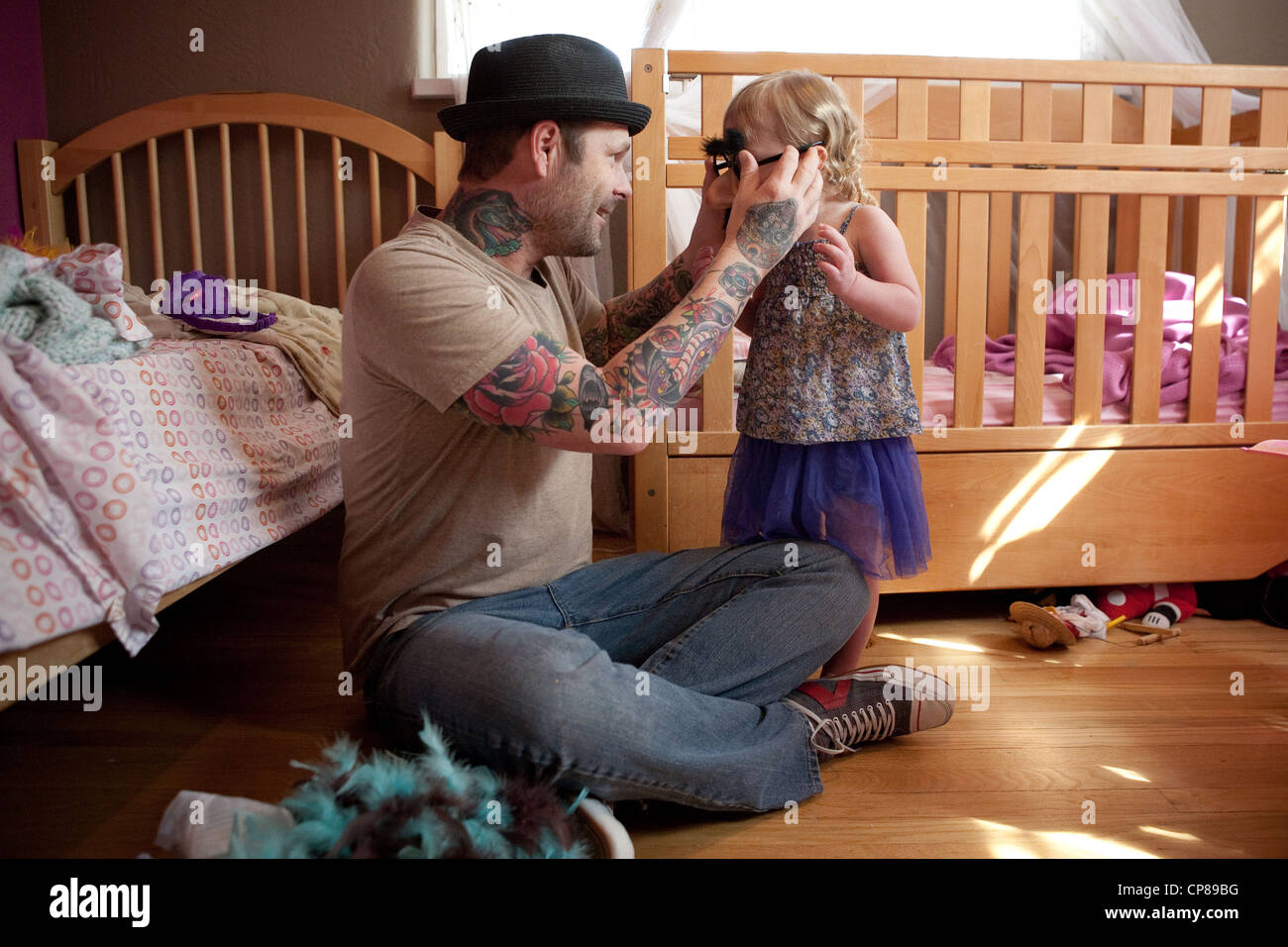 Vater mit Tattoo auf Arme spielt mit seiner Tochter in ihrem Schlafzimmer, dumme vorgeben Schnurrbart und Brille anprobieren. Stockfoto