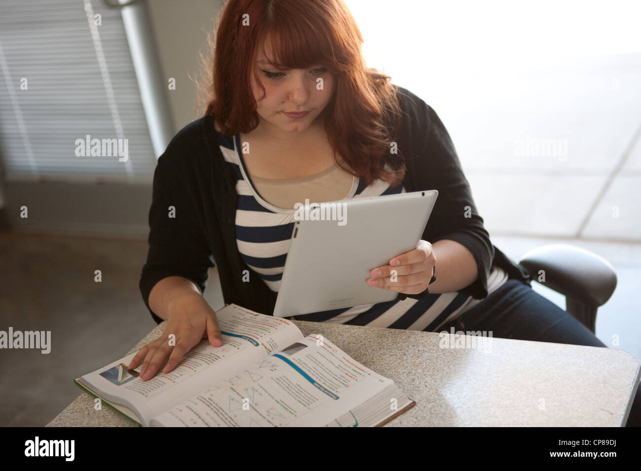 Fünfzehn Jahre altes Mädchen in USA Mathe Hausaufgaben mit Lehrbuch und ein Ipad. Stockfoto