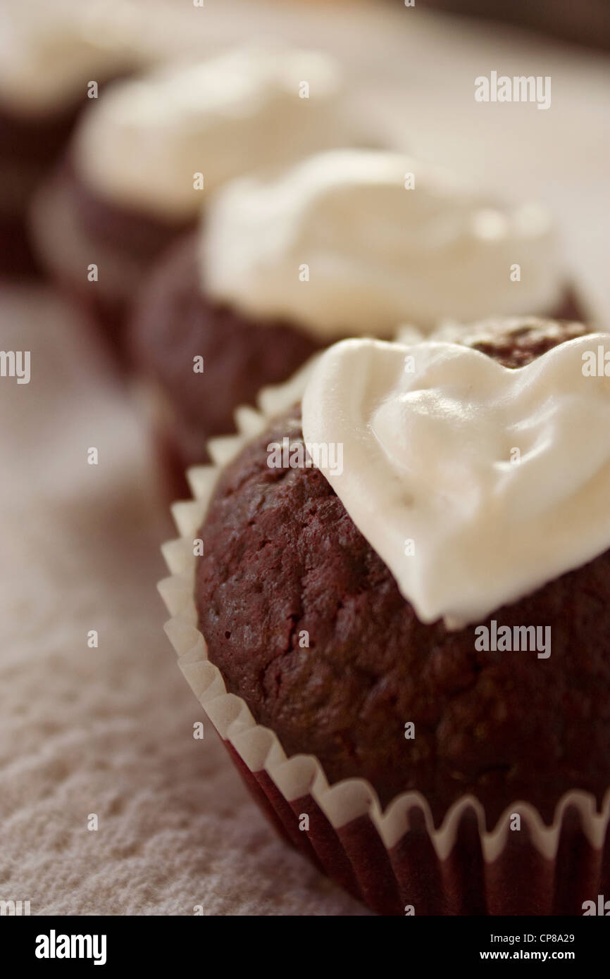 Red Velvet Cupcakes mit herzförmigen Sahnehäubchen sind auf einem Tisch aufgereiht. Essbare Valentine Geschenke. Stockfoto