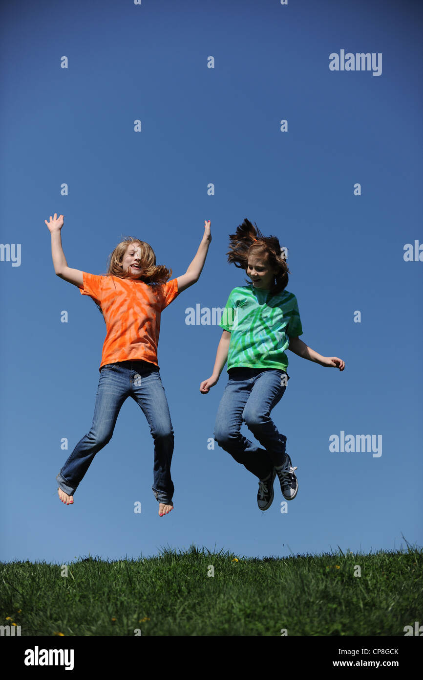 Zwei junge Mädchen, die an einem sonnigen Tag vor einem blauen Himmel springen Stockfoto