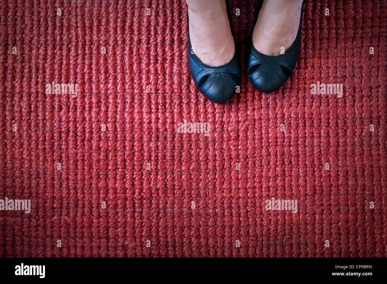 Schwarze Pumps auf einem strukturierten roten Teppich. Stockfoto