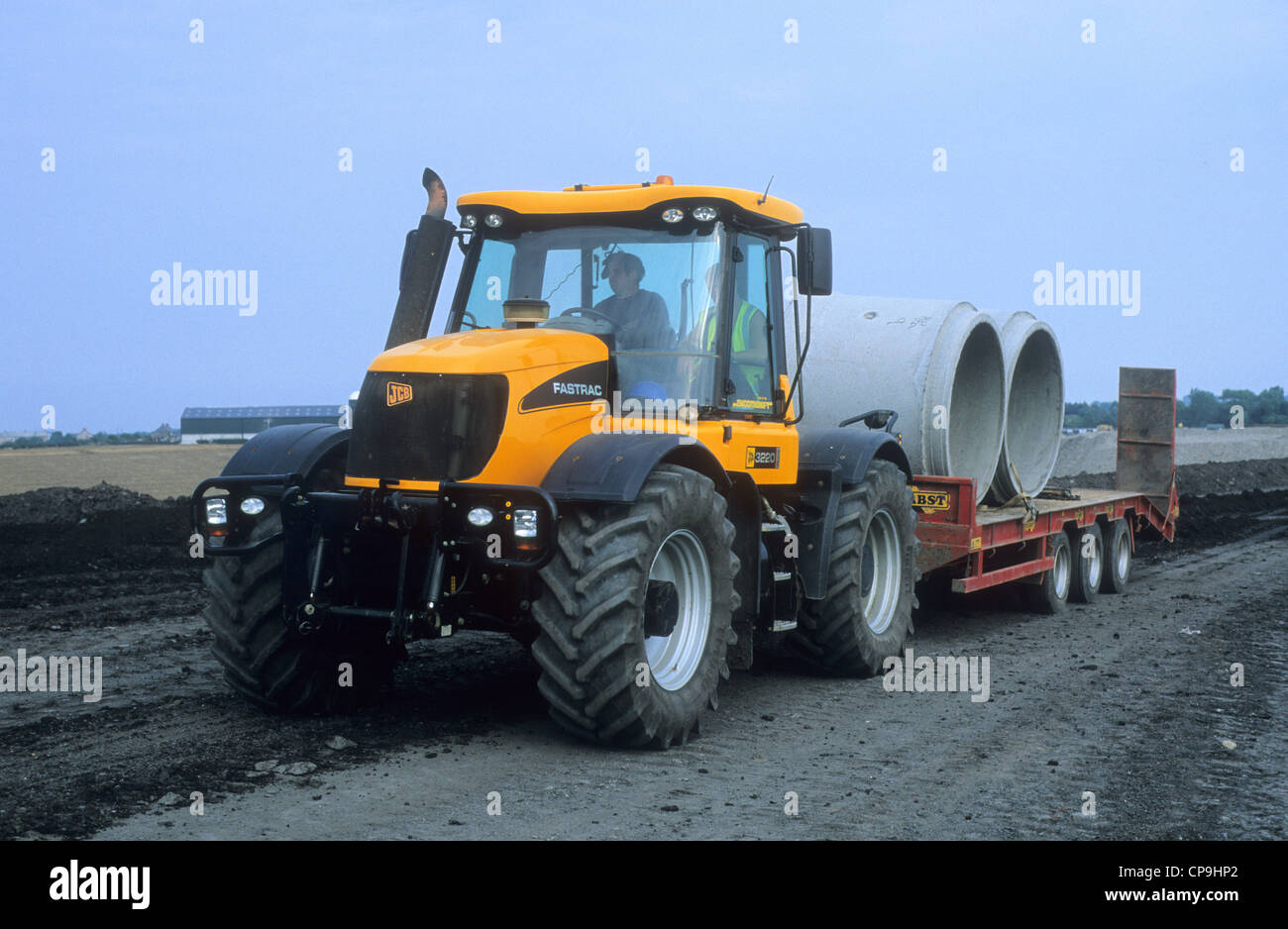 Ein "JCB Fastrac 3220" Baufahrzeug Abschleppen Beton Rohre Rohre über ein Land re Entwicklung vor Ort. Stockfoto