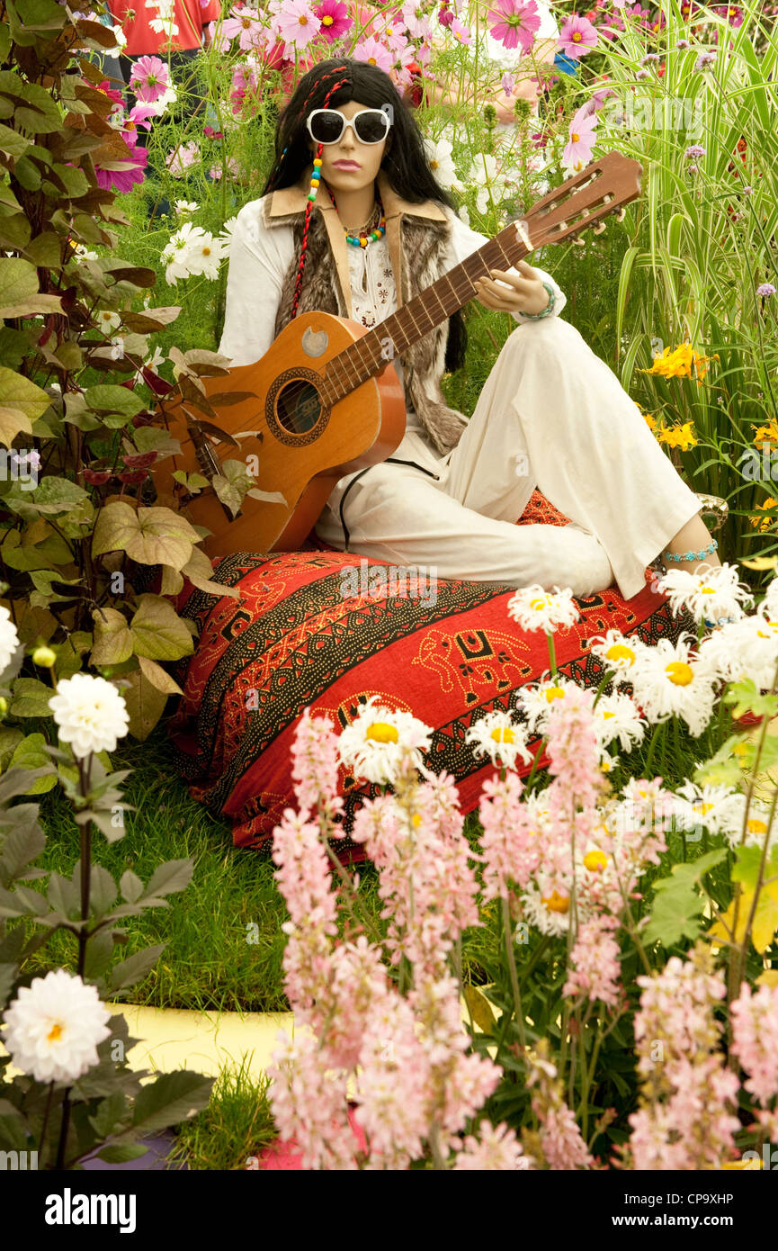 60Er flower power Gestalt mit Schattierungen, Gitarre, sitzen auf Kissen von farbenfrohen Blumen - RHS Flower Show, Tatton Park, Cheshire, Großbritannien Stockfoto