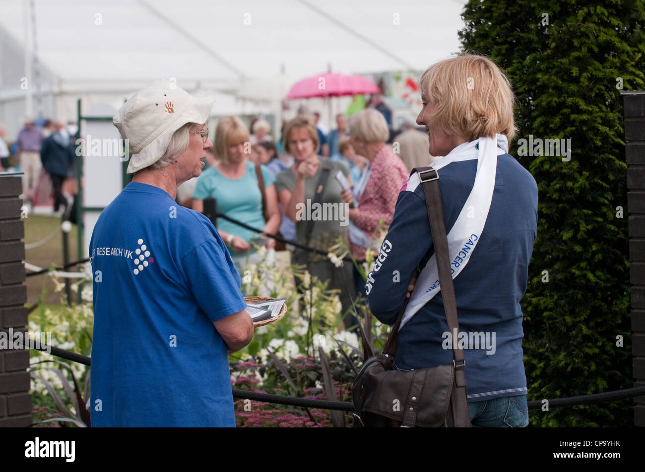 Die Menschen/-Garten für Krebsforschung Großbritannien als weibliche Freiwillige steht im Gespräch mit Designer-RHS Flower Show, Tatton Park, Cheshire, England. Stockfoto