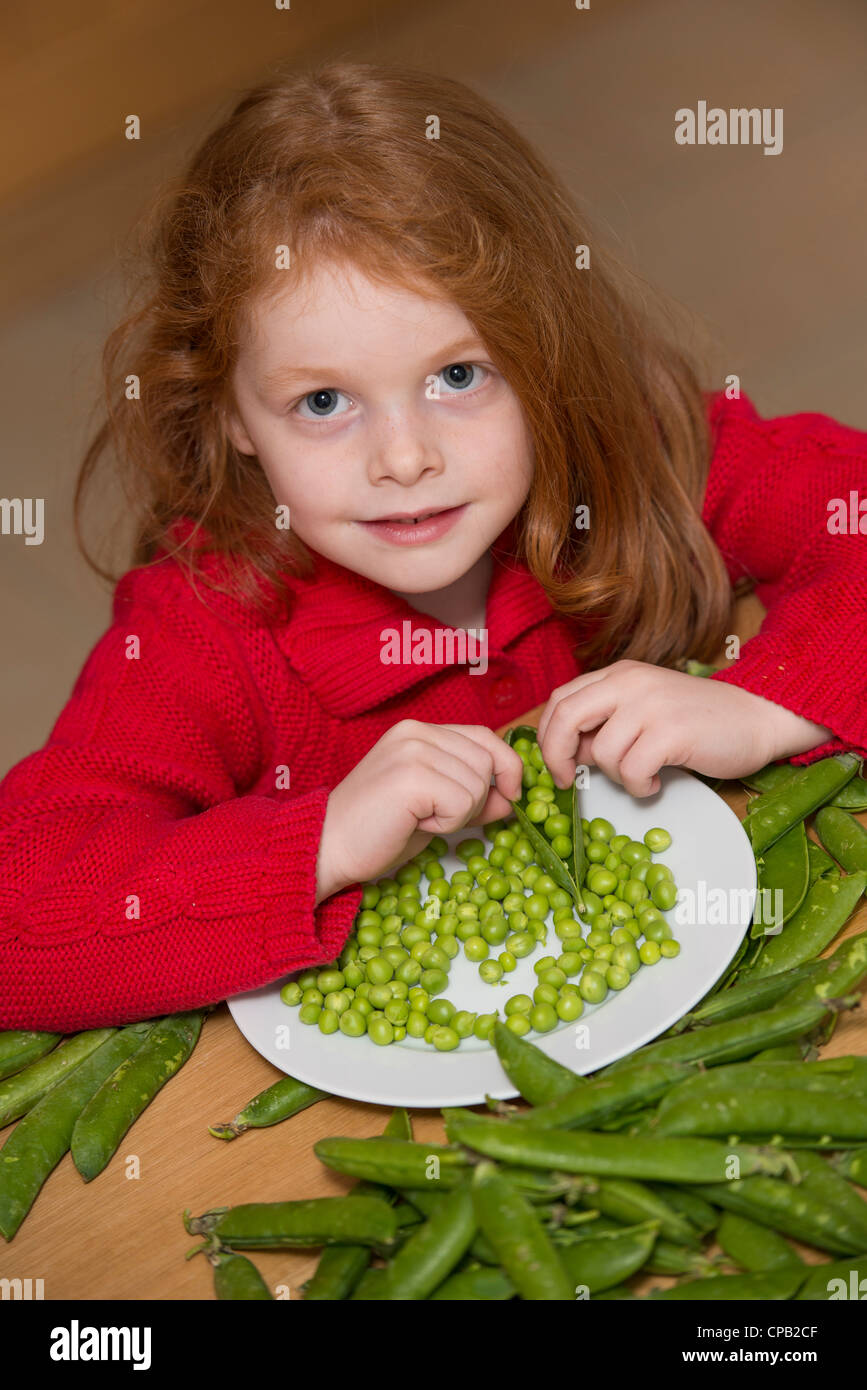 Kind schälen Erbsen auf einem Küchentisch Stockfoto