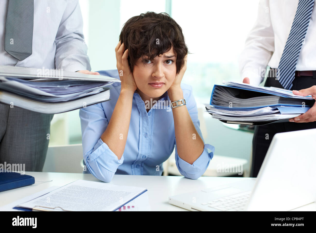 Verängstigte Sekretärin berühren den Kopf beim Blick in die Kamera, umgeben von großen Haufen von Papieren Stockfoto