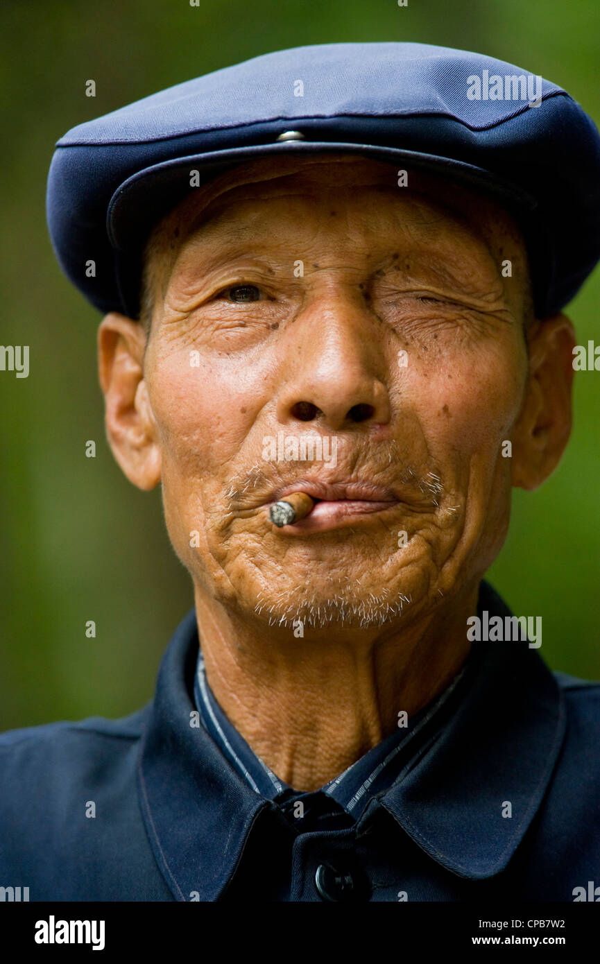 Eine ältere chinesische Mann in traditioneller Kleidung und das Rauchen eine Zigarre posieren für die Kamera in Pingliang gekleidet. Stockfoto