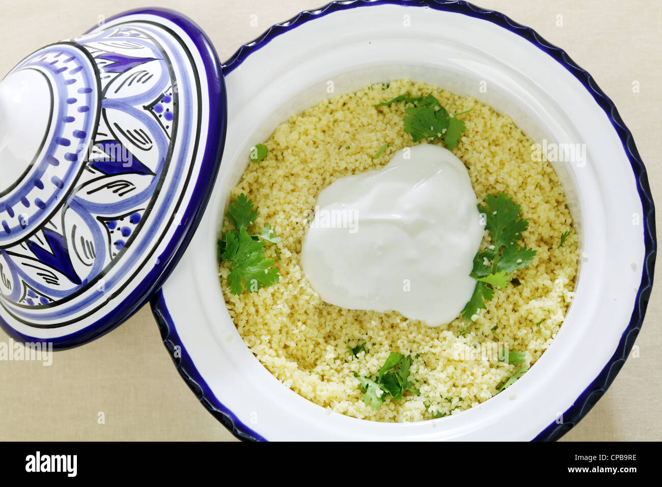 Eine nordafrikanische Keramik Tajine Schale voll Couscous, garniert mit frischen Joghurt und mit Koriander garniert Stockfoto