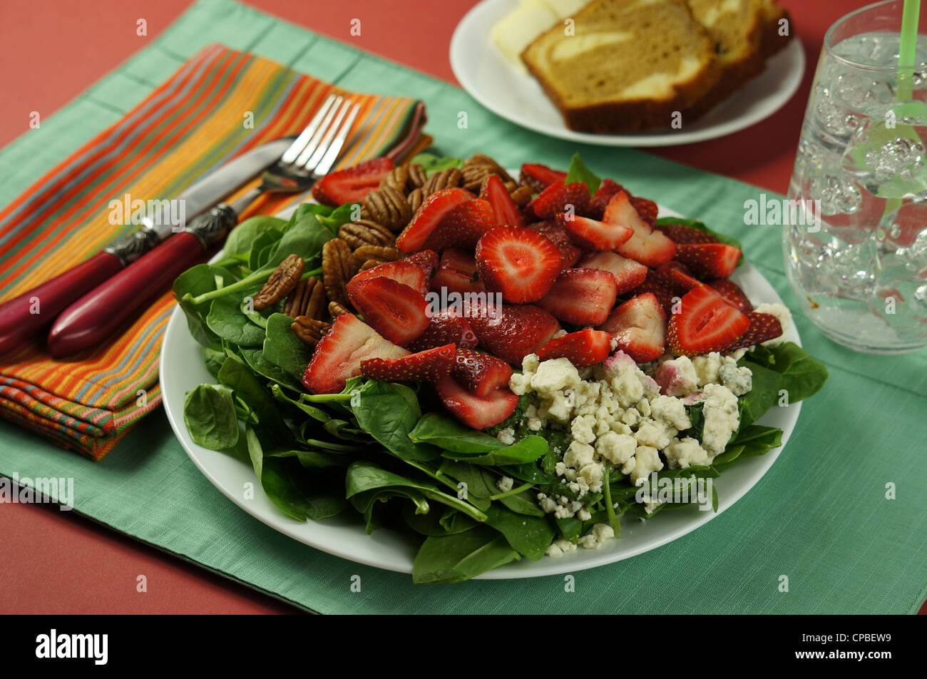 Spinat Mittagessen Salatteller mit Pekannüssen, Erdbeeren und Blauschimmelkäse, serviert mit Brot Zimt Streusel und Eiswasser. Stockfoto