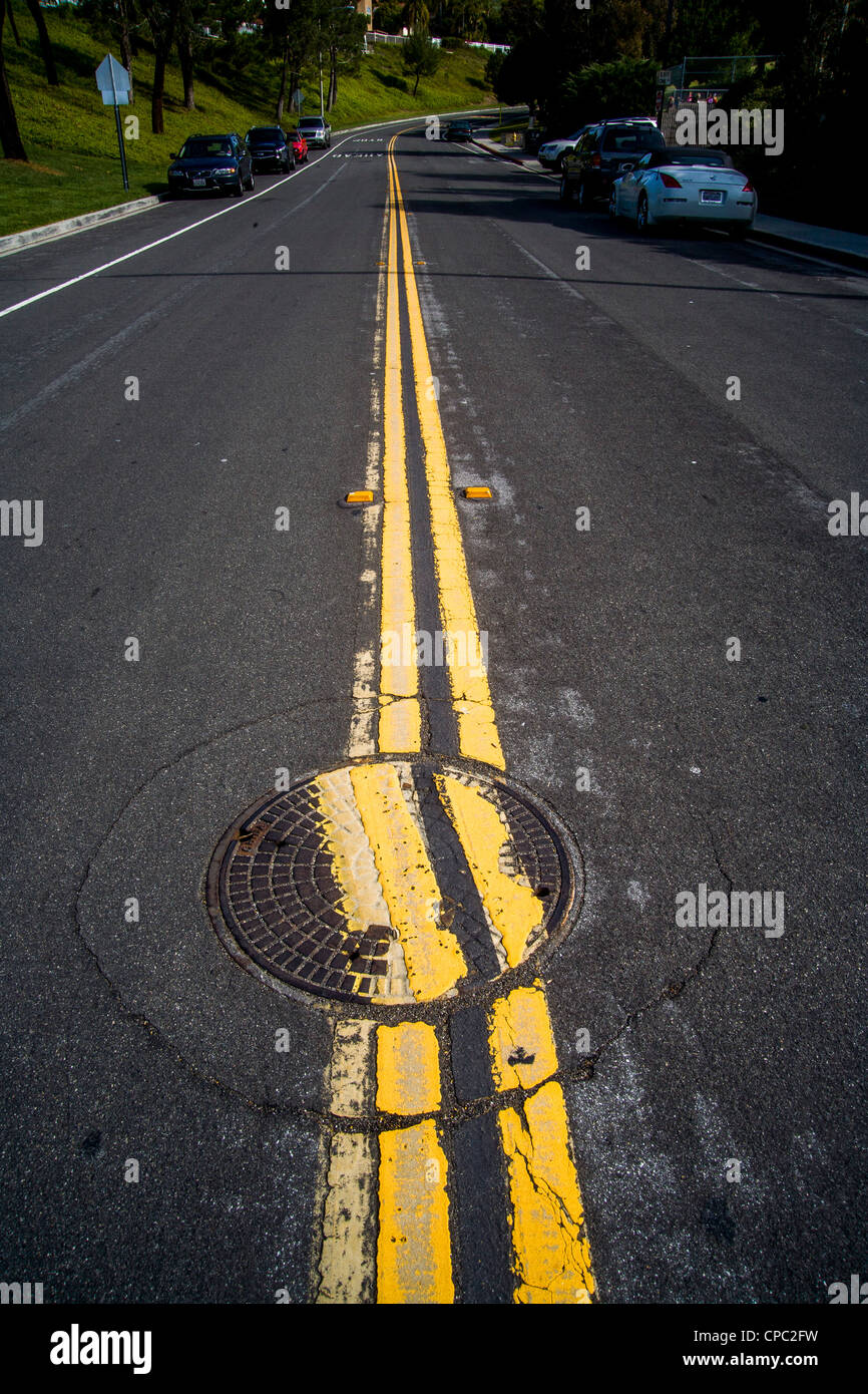 Ein achtlos ersetzte Schachtdeckel unterbricht zwei parallele Linien auf einer Straße in San Clemente, Kalifornien. Stockfoto