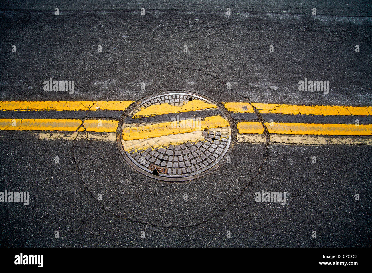 Ein achtlos ersetzte Schachtdeckel unterbricht zwei parallele Linien auf einer Straße in San Clemente, Kalifornien. Stockfoto
