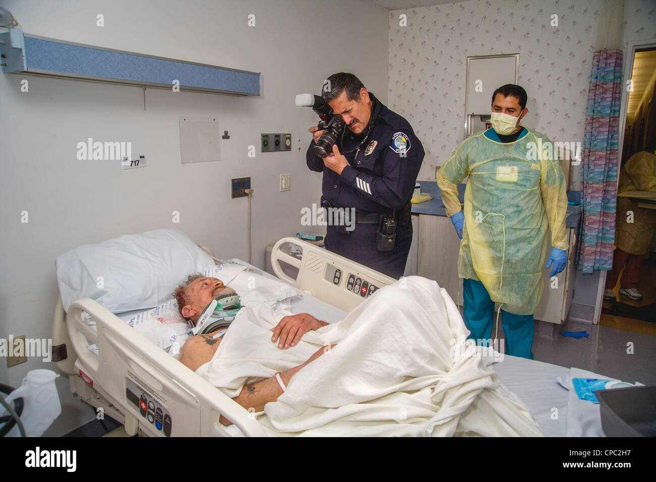 In einem örtlichen Krankenhaus fotografiert eine Hispanic Polizei Kriminalität Ermittler Verletzungen zu einem älteren Obdachlosen Angriff Opfer. Stockfoto