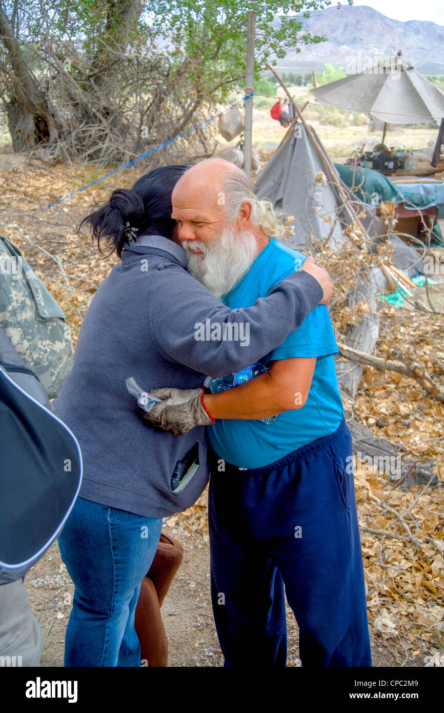 Hispanische Nächstenliebe Vertreter schmiegt sich eine Obdachlose militärischen Veteran auf ein Outdoor-Lager in der Wüste Stadt Victorville, CA. Stockfoto