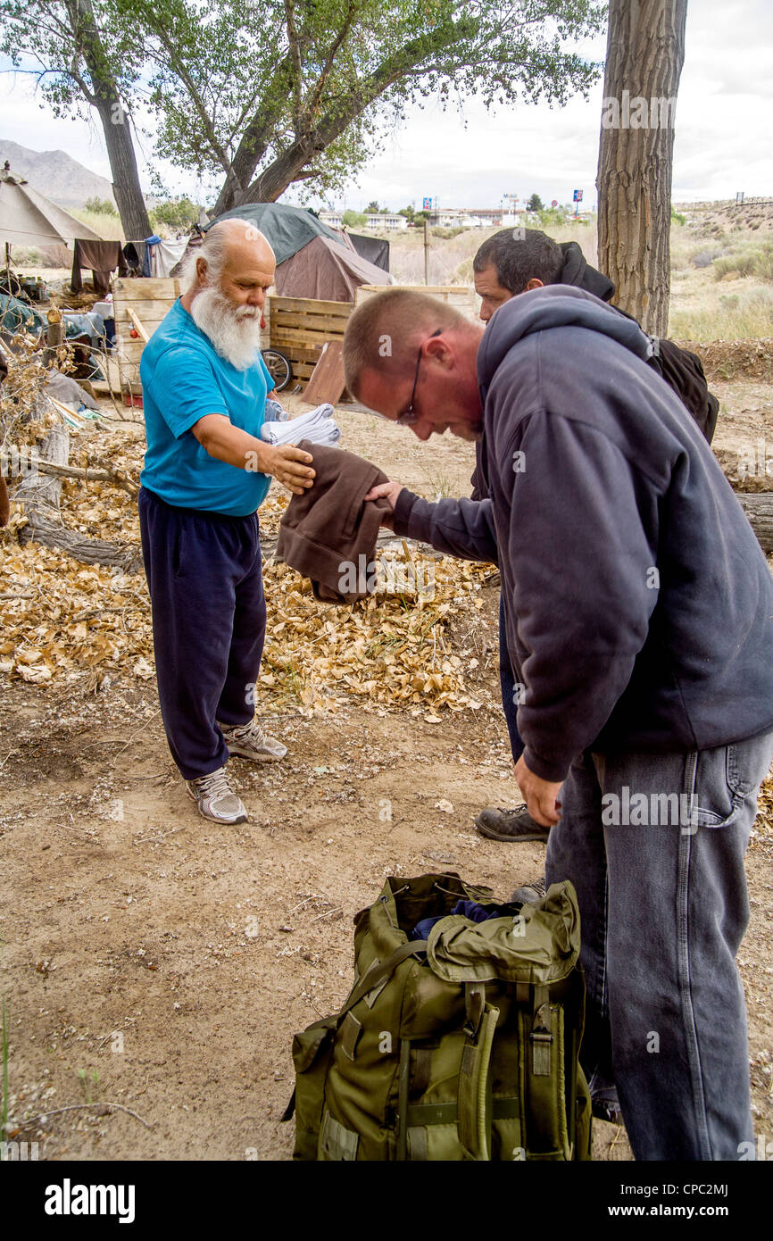 Nächstenliebe Arbeiter bietet ein Obdachloser eine Auswahl an freien Kleidungsstücke in ein Outdoor-Lager in der Wüste Stadt Victorville, CA. Stockfoto