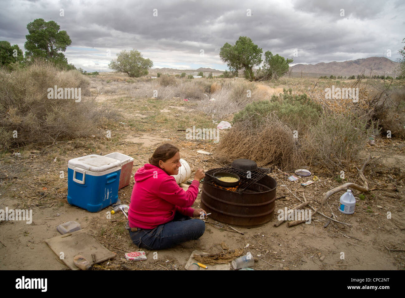 Eine Obdachlose Frau kocht Mais auf einem primitiven Außengrill einem primitiven Outdoor-Lager in der Wüste Stadt Victorville, CA. Stockfoto