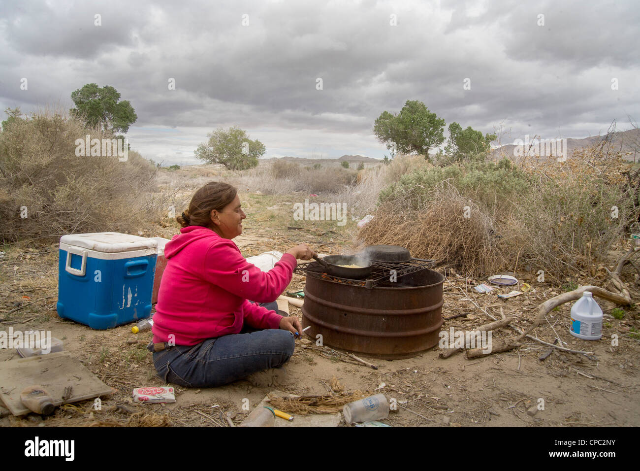 Eine Obdachlose Frau kocht Mais auf einem primitiven Außengrill einem primitiven Outdoor-Lager in der Wüste Stadt Victorville, CA. Stockfoto